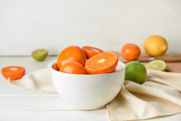 Bowl with healthy citrus fruits on light wooden background