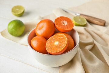 Bowl with healthy citrus fruits on light wooden background