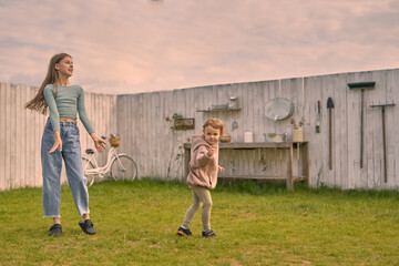 two girls sisters in the backyard of a country house play and dance against the background of a wooden white fence