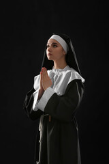 Young praying nun on dark background