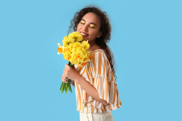 Beautiful young African-American woman with narcissus bouquet on color background