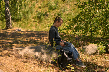 Naklejka na ściany i meble a young girl in nature in the forest sits on a rock and communicates online on the Internet via a laptop