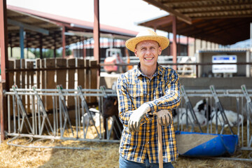 Positive american Male farmer in strow hat posing against background of cows in stall