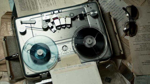 Audio tape records on table covered in documents as room light blinks, reveal