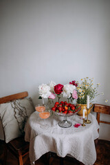 plate with fresh strawberries on the table with flowers and two glasses. table with peonies and daisies in vases. italian peach cocktail in transparent glasses near a fruit plate with strawberries.