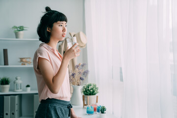 attractive young asian chinese woman drinking glass of water at home living room. beautiful girl...