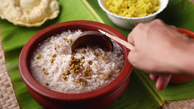 Rice porridge, Kanji gruel clay pot on banana leaf  4K slow motion video footage Kerala South India. woman hand serve congee rice soup green gram curry Ayurveda diet immunity Indian Sri lanka veg food