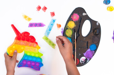 Children's toy popit unicorn of rainbow colour from soft plastic. Kid's hands paint bauble by colour. Other use of toy unicorn ice cube trays. Entertainment for children. Make coloured ice homemade.