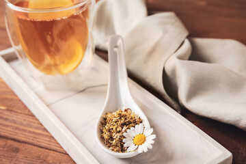 Spoon with dried chamomile and cup of tea on wooden background