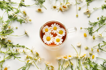 Composition with cup of chamomile tea and flowers on light background