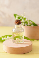 Obraz na płótnie Canvas Bottle with essential oil and lily-of-the-valley flowers on color wooden background