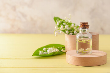 Bottle with essential oil and lily-of-the-valley flowers on color wooden background