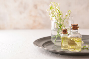 Bottles with essential oil and lily-of-the-valley flowers on light background