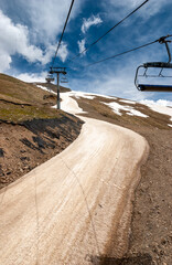 A winding river of dusty brown snow and a cable car on the slopes of Dombay. Caucasus, Russia.