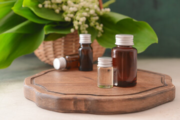 Bottles with essential oil and lily-of-the-valley flowers on light background