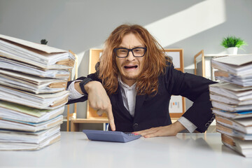 Crazy male accountant sits among the folders with documents and nervously presses buttons on the calculator. Emotional man is full of anger and bad feelings. Concept of stress at work.