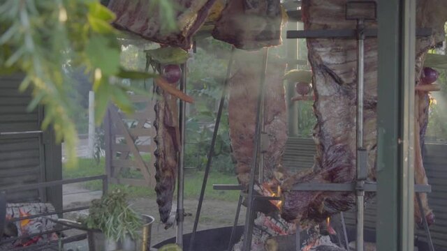Slow motion handheld shot of raw meat asado being cooked and smoke passing by