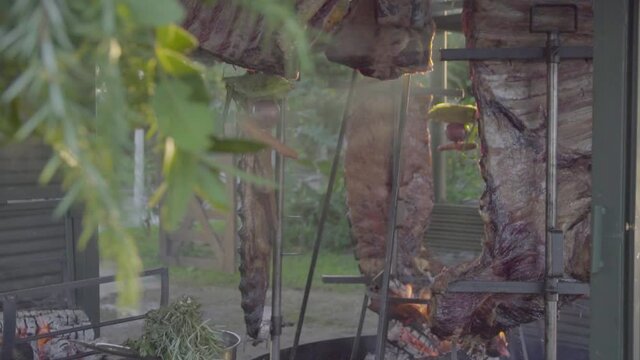 Slow motion handheld shot of raw meat asado being cooked and smoke passing by