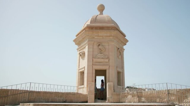Couple getting out of the guard tower in Gardjola Gardens. The view of the Senglea Guard tower with sculpted symbols (crane bird, ear and nose) in the early morning light. Senglea, Malta.