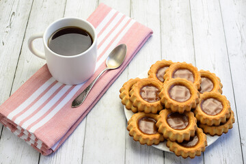 White cup with tea, teaspoon on a kitchen napkin, homemade cookies on a light wooden background. Concept of home breakfast, afternoon tea. Tea ceremony. Side and top view.