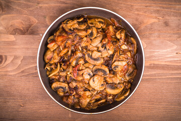 Homemade stew of tomatoes and champignon mushrooms in a plate on the table, top view, close-up