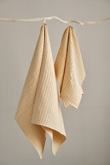 Collection of natural muslin kitchen towels are hung in a row on an unusual wooden hanger. Natural, soft, airy and stylish kitchen textiles. Front view.