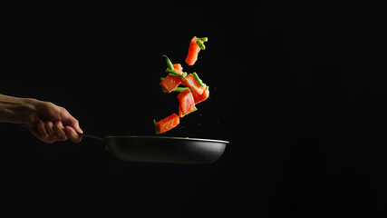 Beautiful still life. Pieces of red fish and greens in a frying pan in a state of levitation. Contrast - bright colors of fish and greenery and a black background. Focusing on the foreground.
