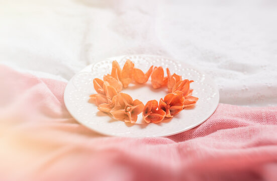 A white plate with dry fragrant flowers on the table in folds of pink fabric. 