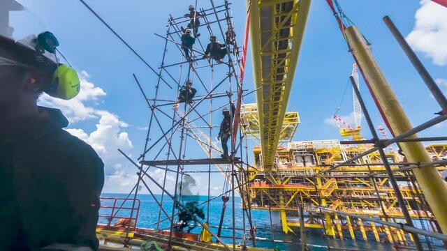 4K time lapse low angle view of scaffold erectors working at height at gas platform for scaffold erection works.