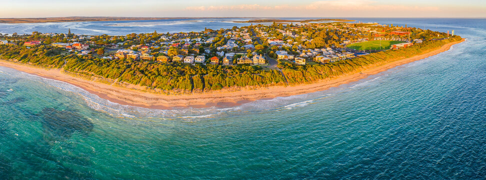 Aerial panoramic view of a sandy beach and coastal town stretching along a peninsula at sunset