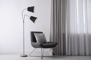 Comfortable armchair with cushion and floor lamp near white wall indoors