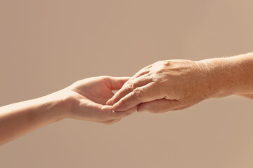 Helping hands on beige background, closeup. Elderly care concept