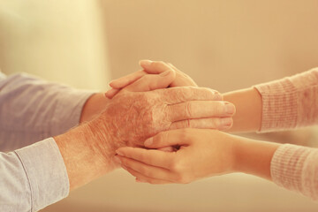 Helping hands on blurred background, closeup. Elderly care concept