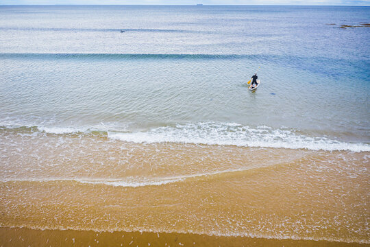 Aerial view of a stand up paddle boarder rowing out to sea over small waves