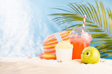 Tropical rest on exotic sea beach with cold drink, ice cream, apple, sun hat, palm leaves with...