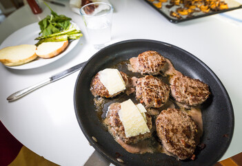 Six hamburger patties in a frying pan.