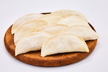 Raw chebureks on a white background, isolated on a round wooden board. The concept of cooking homemade food from meat and dough, raw ice cream semi-finished products