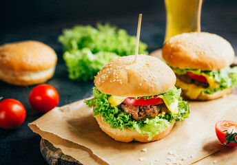close-up of a hamburger with meat on a grill tomato and greens on the background of a glass with beer on a black background