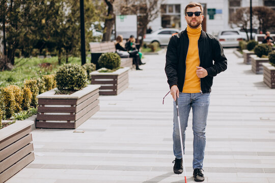 Young handsome blinded man walking with stick in town