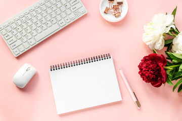 Woman workplace with peony flowers, blank notepad, computer keyboard, computer mouse and pen. Top view, flat lay. Pink background