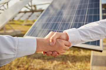 Businessmen shaking hands near solar power station