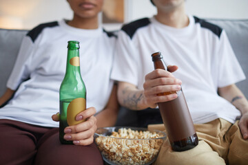 Close up of young couple watching TV or movies at home with focus on pop corn and beer bottles, copy space