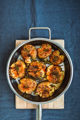 Potatoes baked with rosemary and spices in a frying pan, on a wooden chopping board, blue linen table cloth, top view vertical image