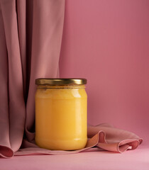 Ghee or clarified butter in jar with pink silk fabric on pink background. Minimal style. Copy space.