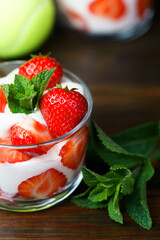 Whipped cream and strawberries served in a glass. Dark wooden table, tennis ball in bokeh, high resolution