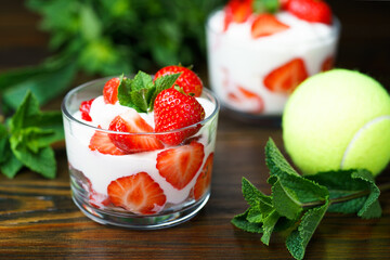 Whipped cream and strawberries served in a glass. Dark wooden table, tennis ball in bokeh, high resolution