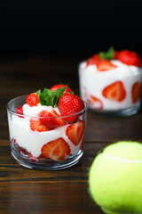 Whipped cream and strawberries served in a glass. Dark wooden table, tennis ball in bokeh, high resolution
