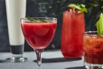 Red Square Cocktail is a classic cocktail with raspberry puree and vodka. Cocktail glass on vintage table with harsh shadow from sunlight. Red cocktail garnished with rosemary sprig.