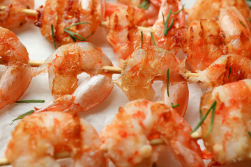 Tasty grilled shrimp skewers on baking paper, close up