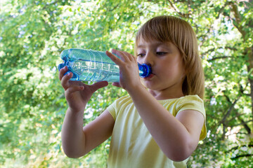  Girl in the summer on a balcony drinks water from a bottle.